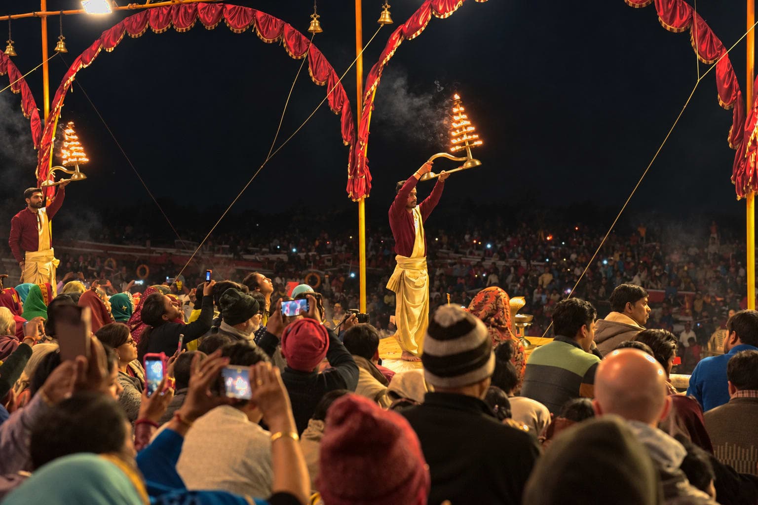 A priest lifts a multi-tiered flaming lamp above the crowd during evening Ganga aarti in Varanasi, 2019