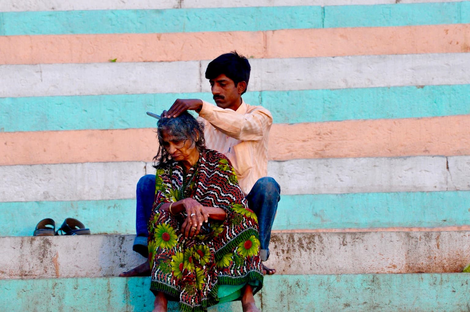 A man tends a seated woman's hair on painted steps of the ghats in Varanasi, photographed in 2014