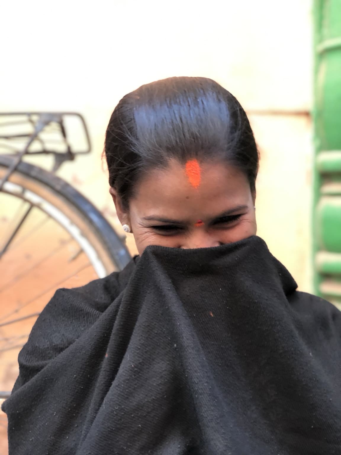 Woman looking down while raising the black shawl across the lower half of her face again.