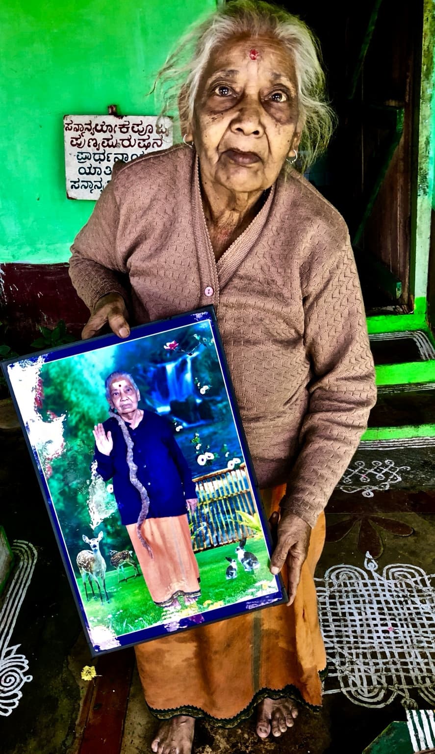 Woman standing in the doorway holding an earlier photograph of herself with long hair.