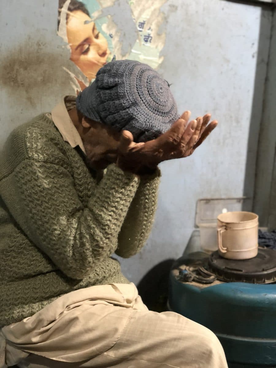 The man seated beside a cup, his head lowered into his hands.