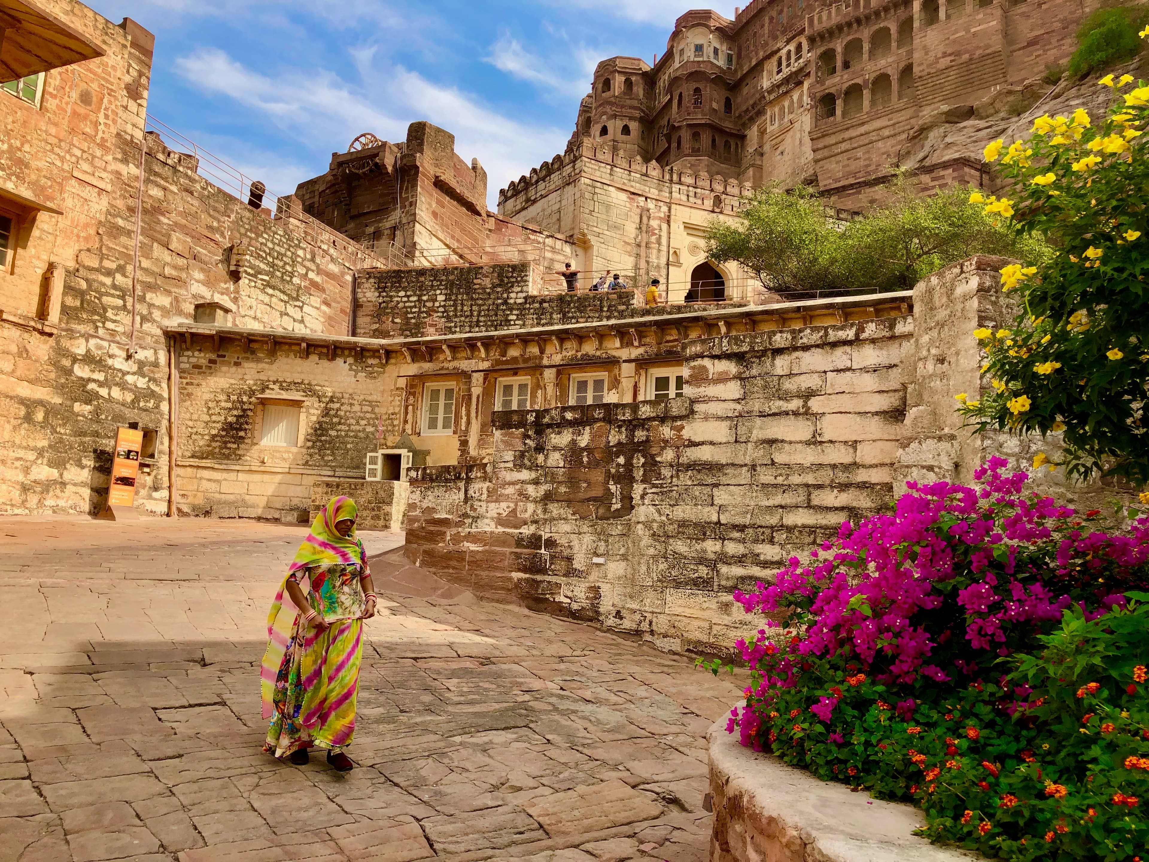 A woman in a colourful sari crosses a stone courtyard beneath Jodhpur’s fort walls.