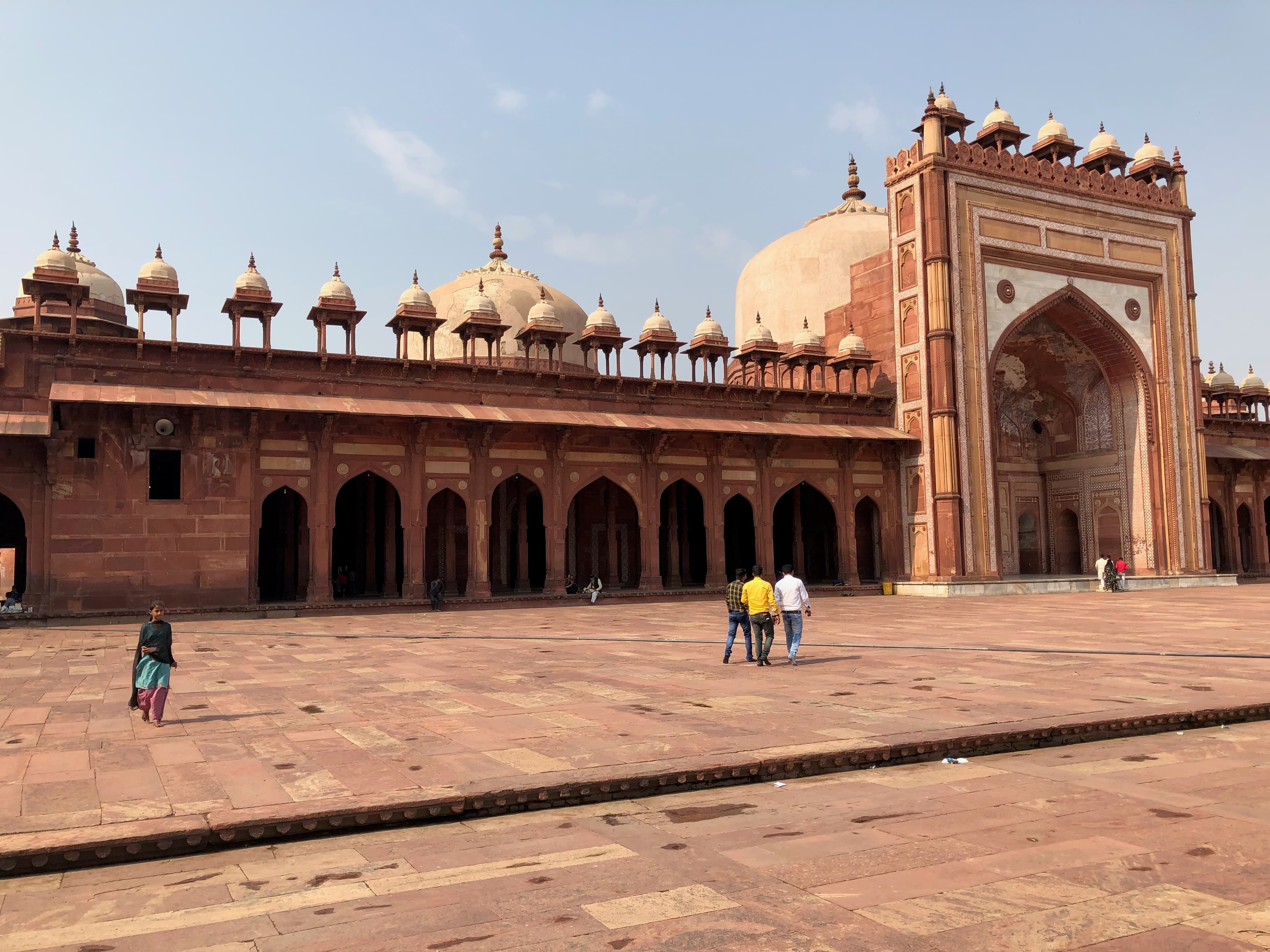 People cross the courtyard beneath the red sandstone arches and domes of Fatehpur Sikri.