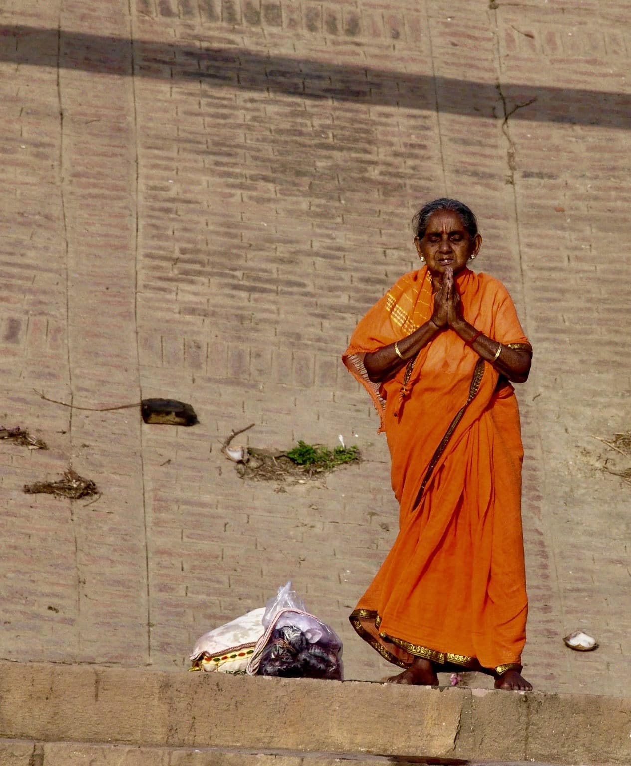 A woman in an orange sari stands in prayer on the stone ghats of Varanasi, photographed in 2014