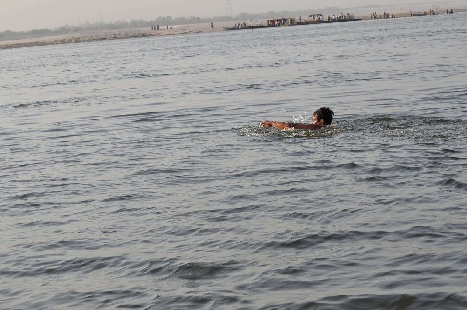 A solitary swimmer surrounded by a broad expanse of the Ganges at Varanasi.