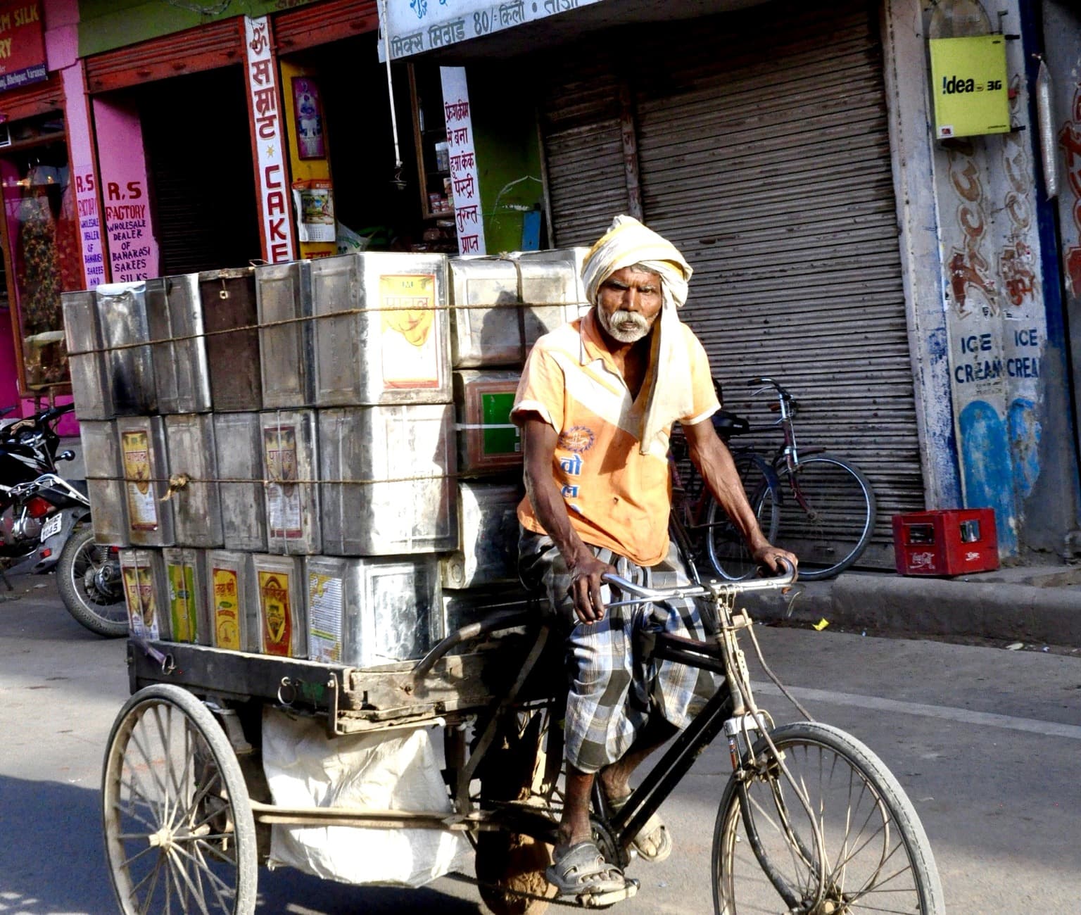 A man transports heavy metal containers by cargo bicycle in Varanasi, photographed in 2014