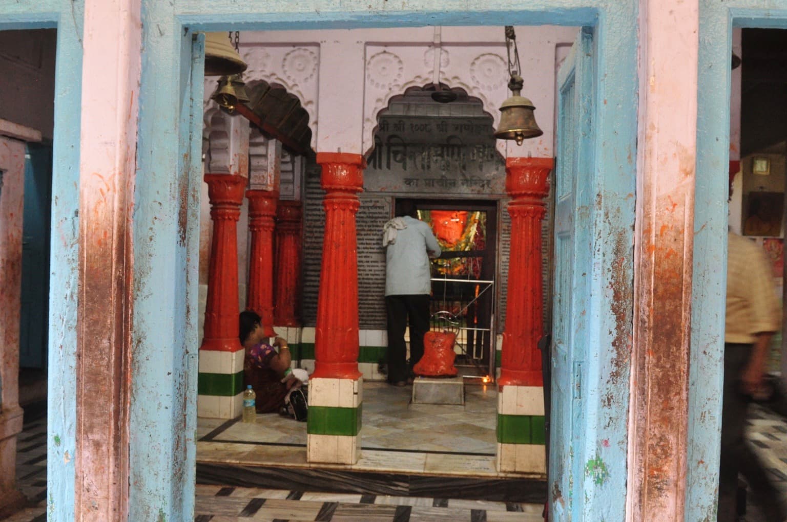 A man prays at a shrine through a weathered blue doorway in Varanasi, photographed in 2014