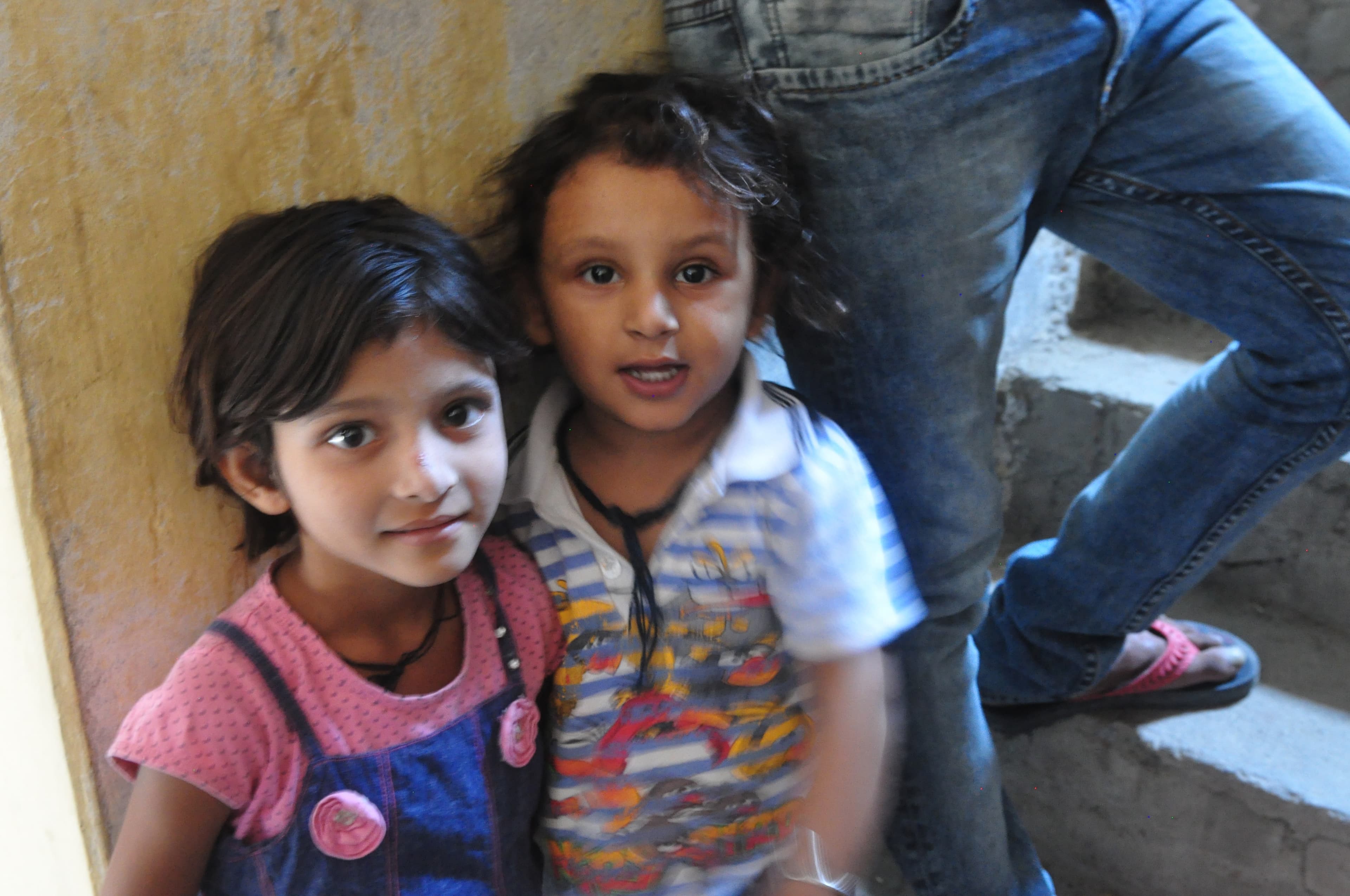 Two children standing together and looking toward the camera inside Baba's home.