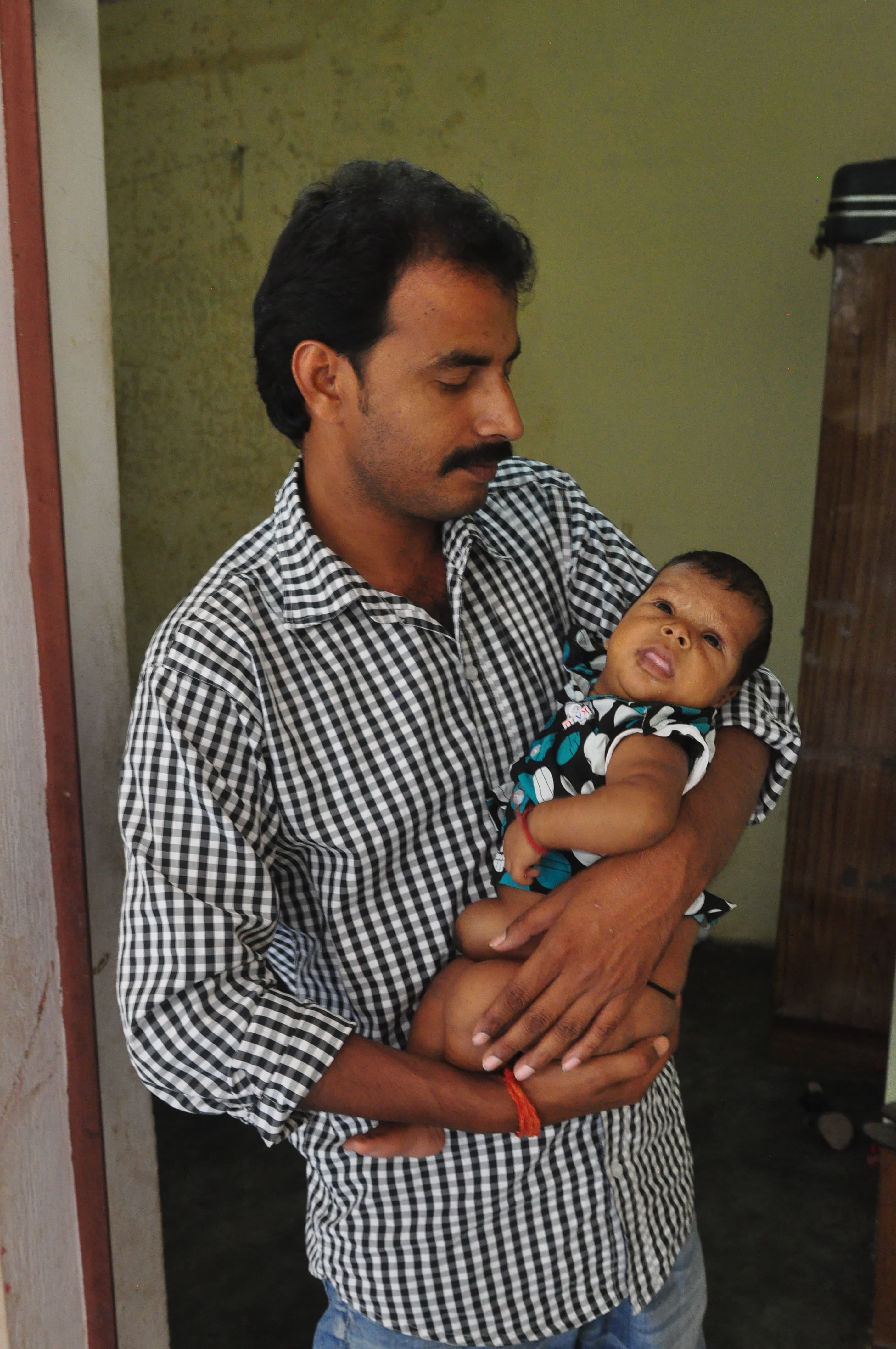 Baba standing in a doorway, holding his child in his arms.