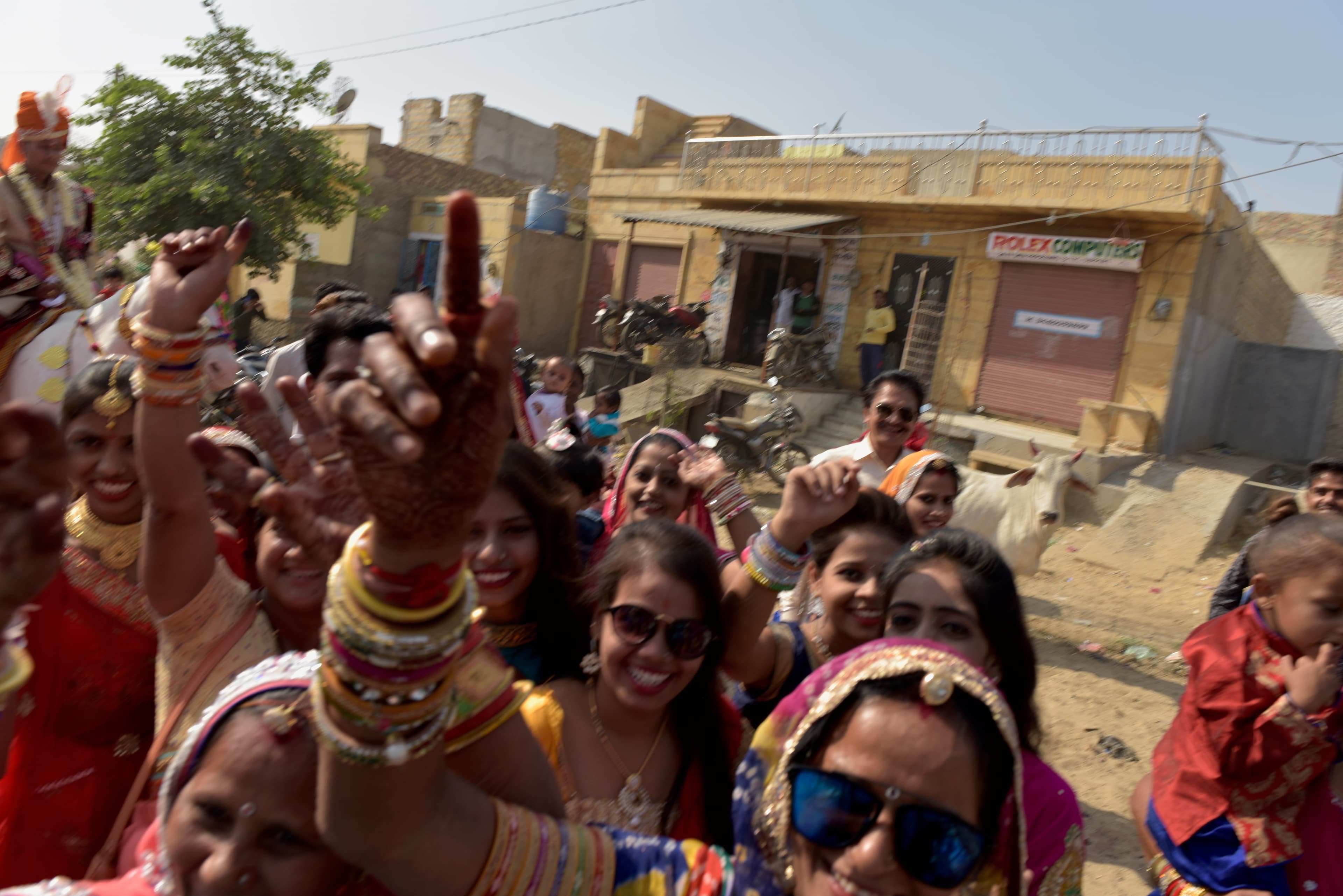 Women smiling and raising their hands toward the camera during the wedding procession.
