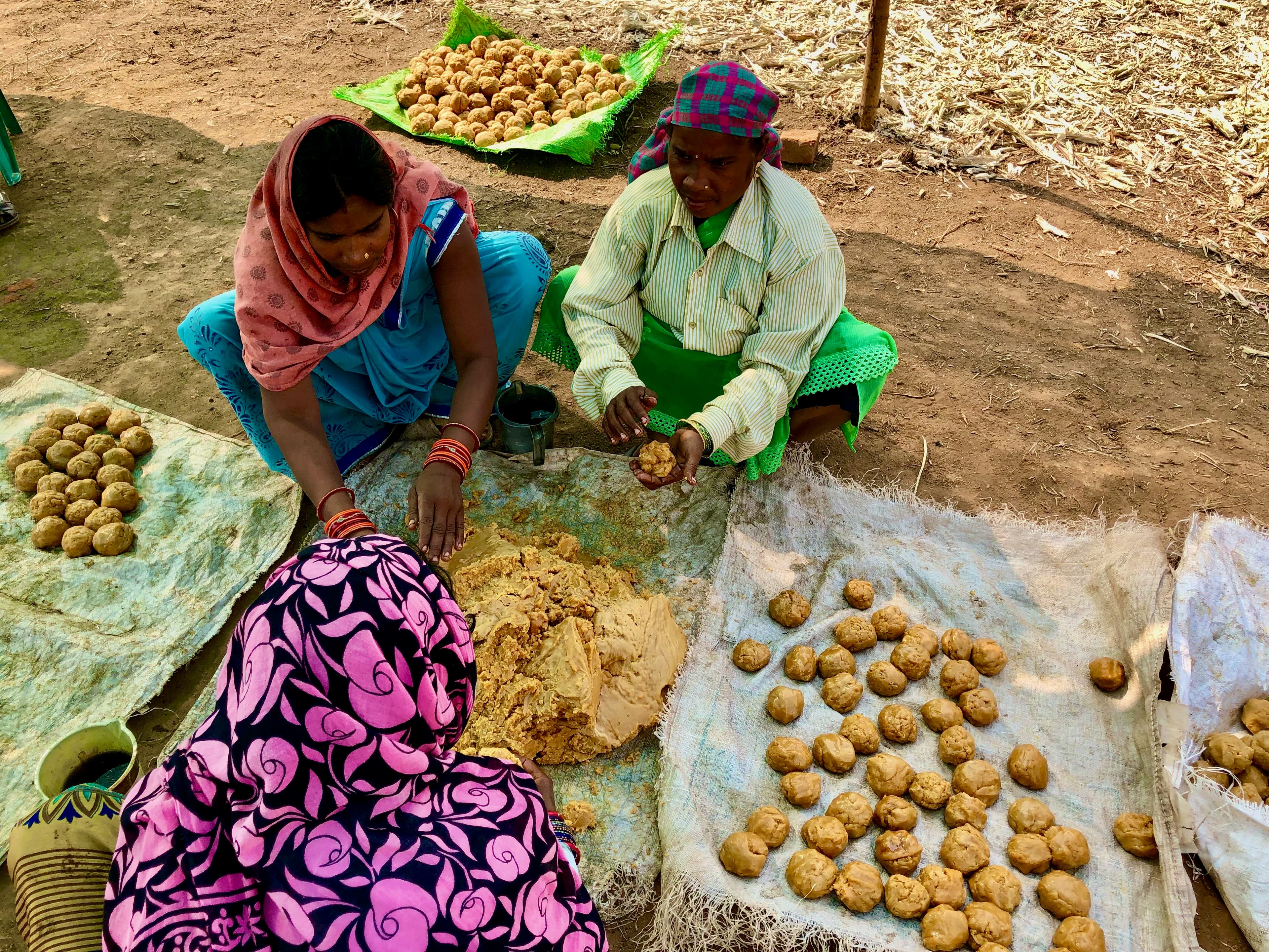 Women shaping portions of jaggery on cloths arranged on the ground.