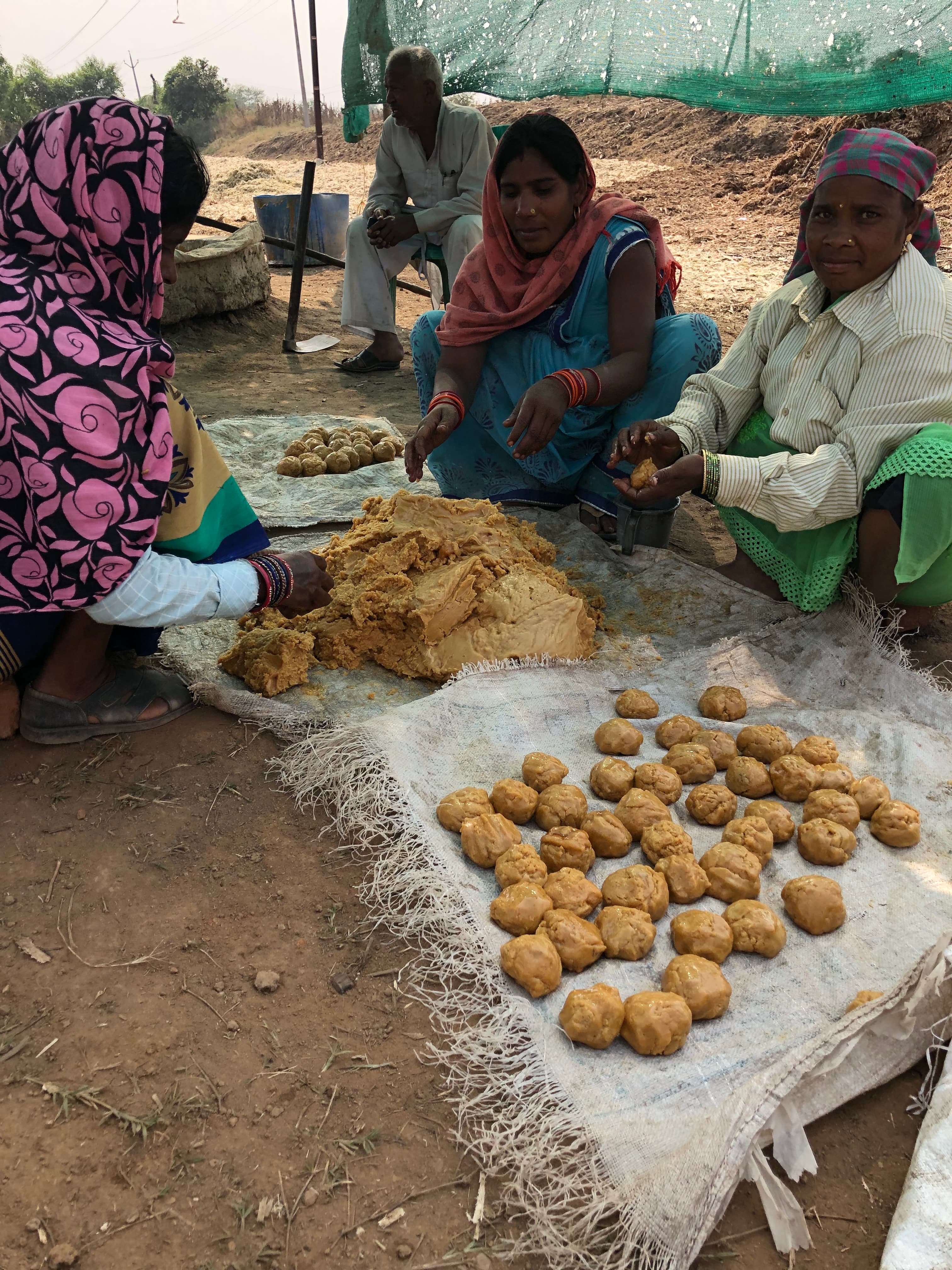 Three women working with jaggery portions as a man sits nearby.